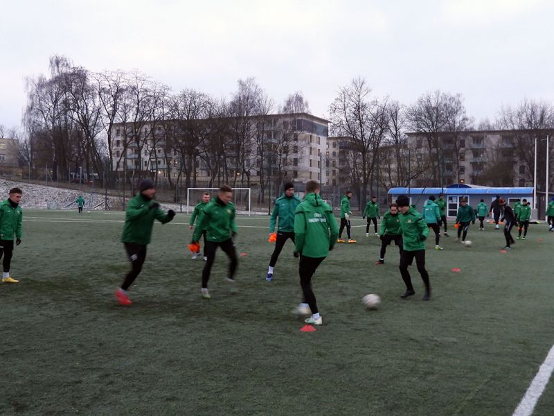 Na zdjęciu piłkarze Lechii podczas treningu. Zawodnicy ubrani w dresy i zielone kurtki klubowe. Trening na murawie boiska